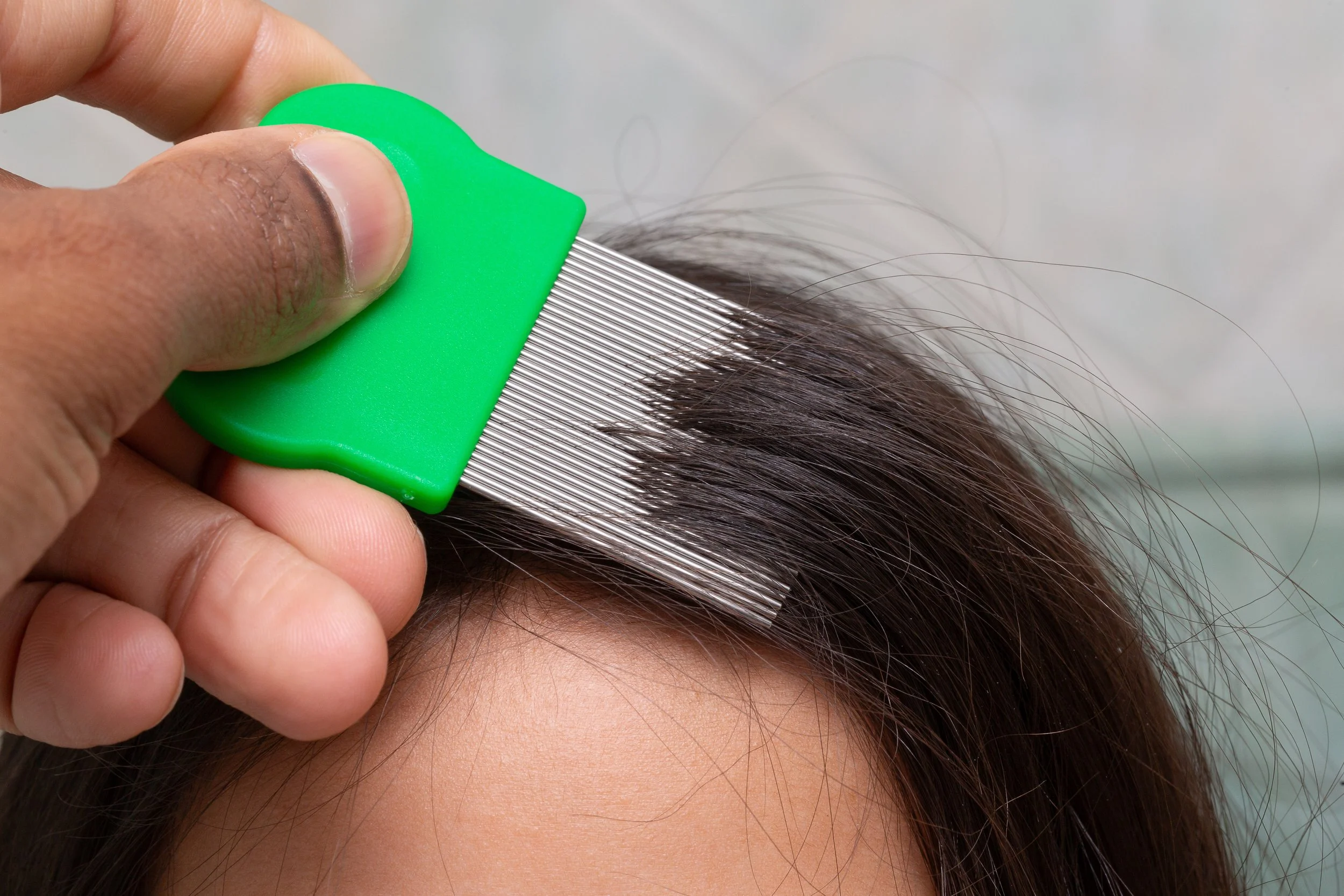 A person holding a green hair clip and parting someone's brown hair to cut or style it.