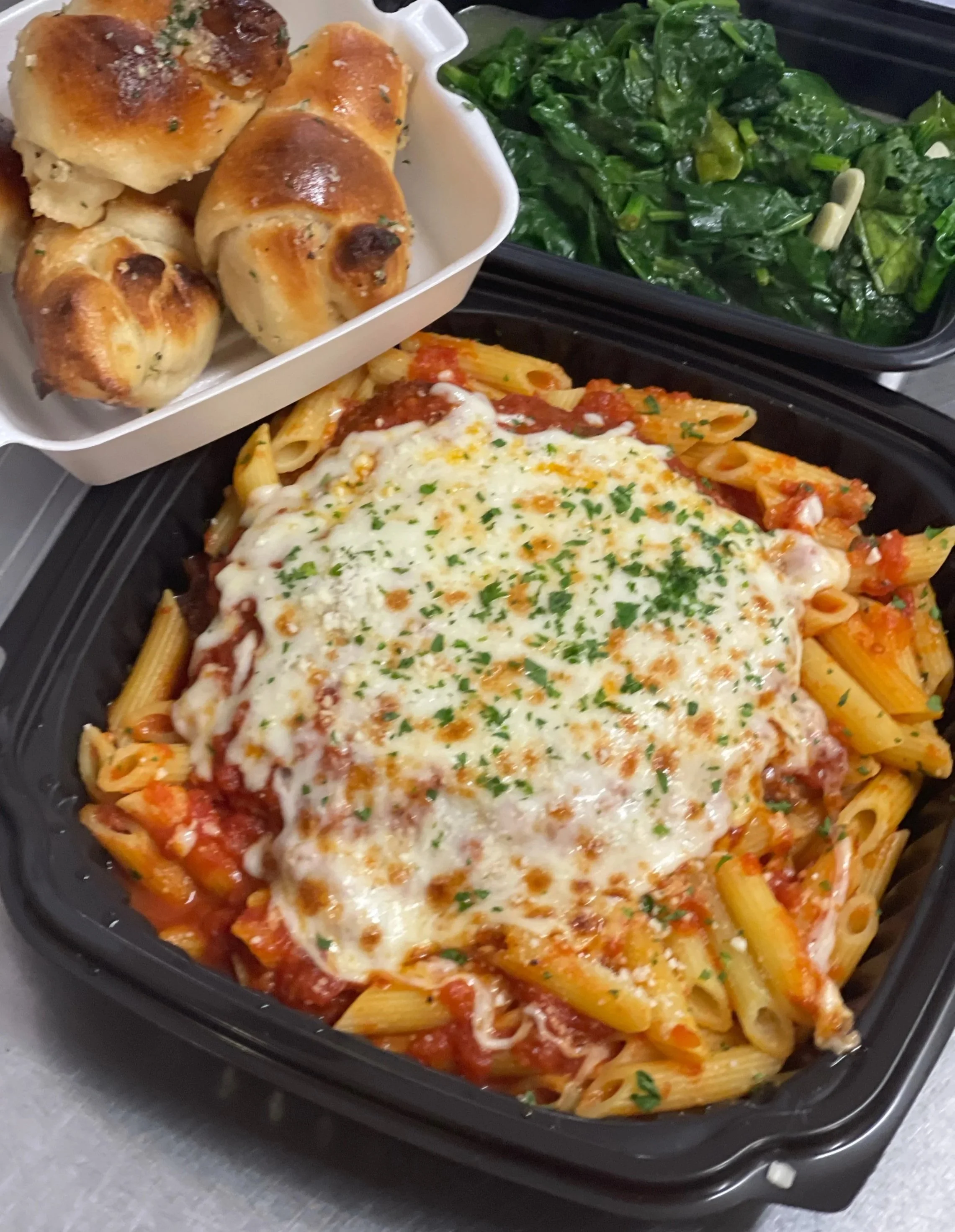 Cooked penne pasta with tomato sauce and melted cheese in a black baking dish.