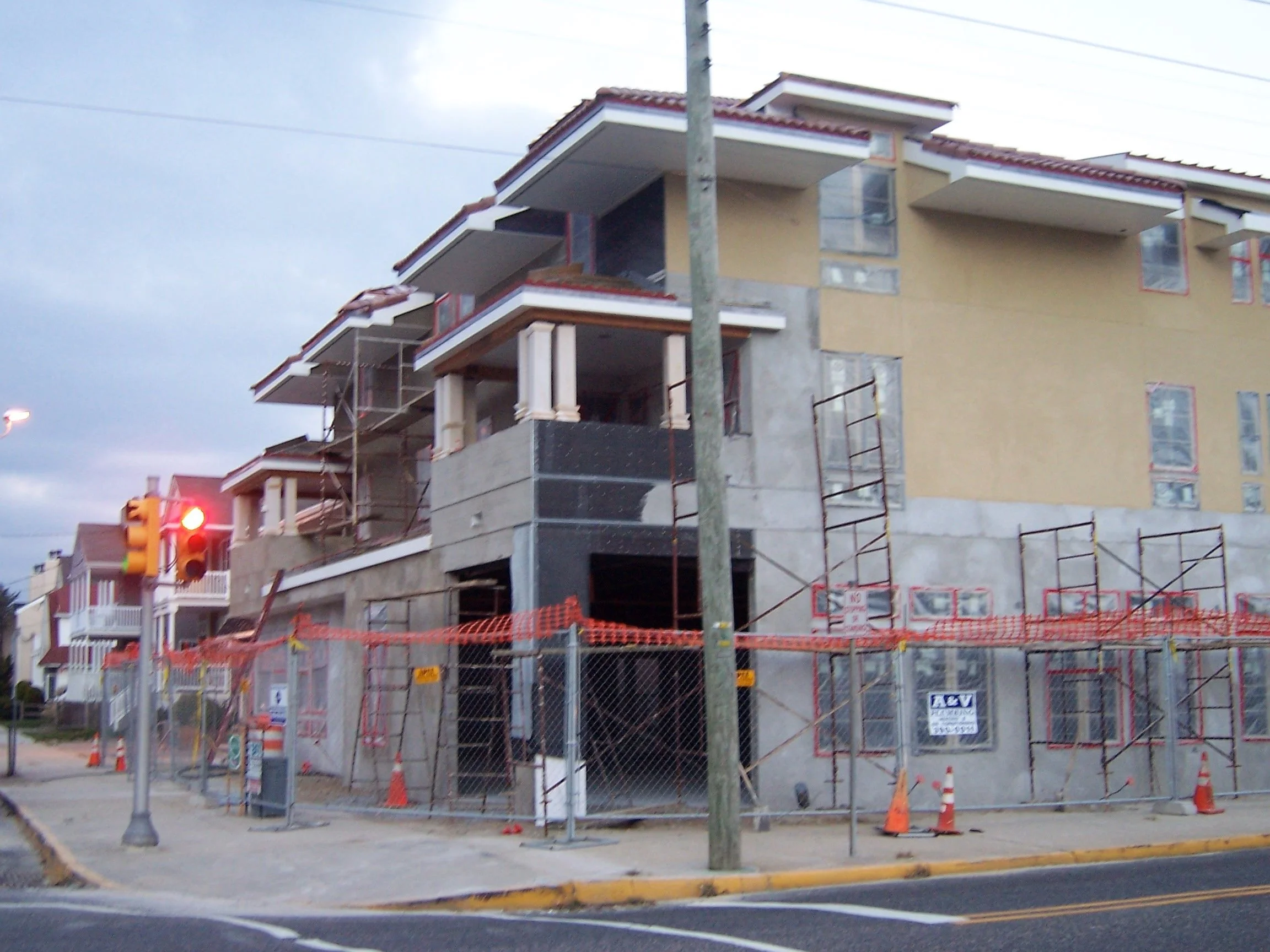 Construction site with a multi-story building under construction, surrounded by scaffolding and orange safety barriers, with a traffic light in foreground.