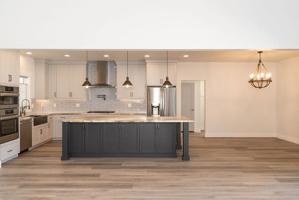 Modern kitchen with white cabinets, a black island, stainless steel appliances, a hanging chandelier, and wood flooring.