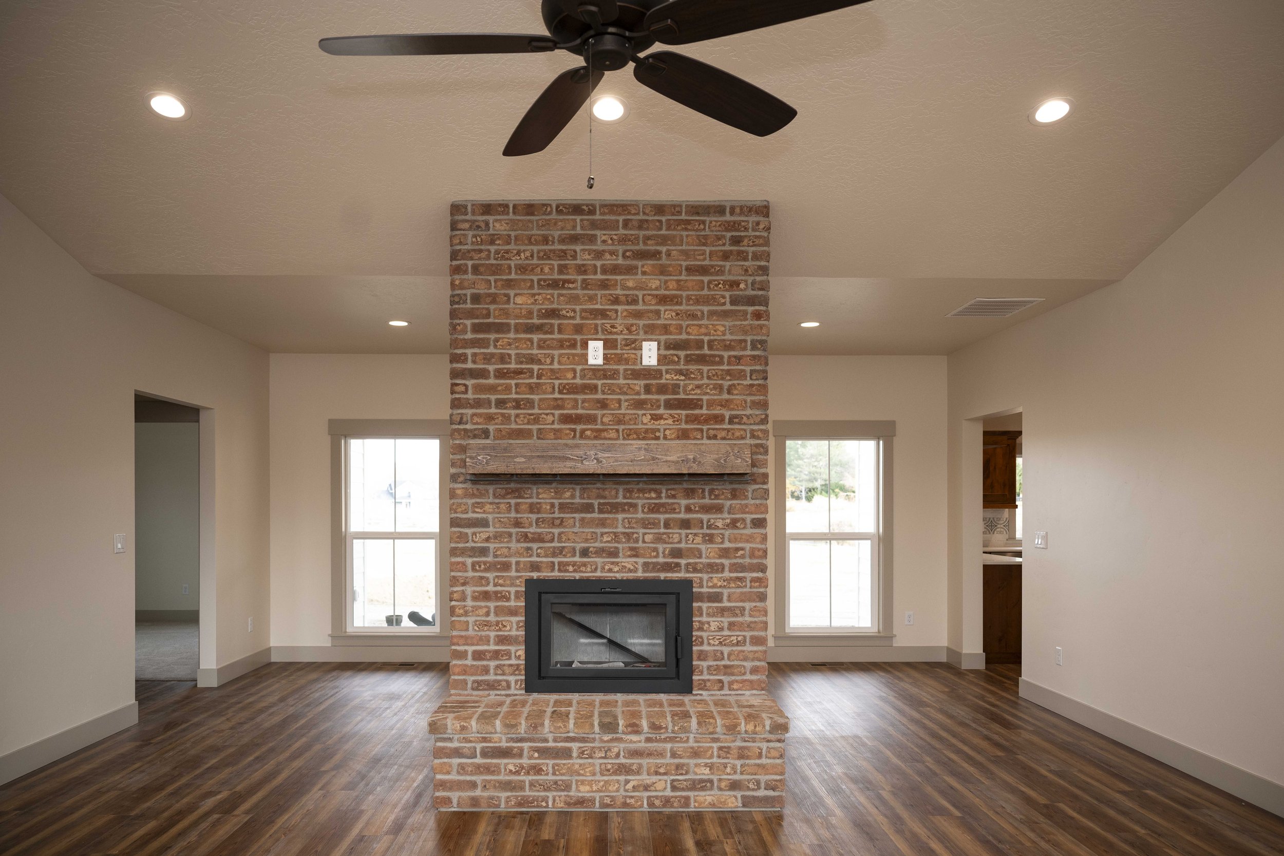 Living room with a brick fireplace, large windows, and wood flooring.