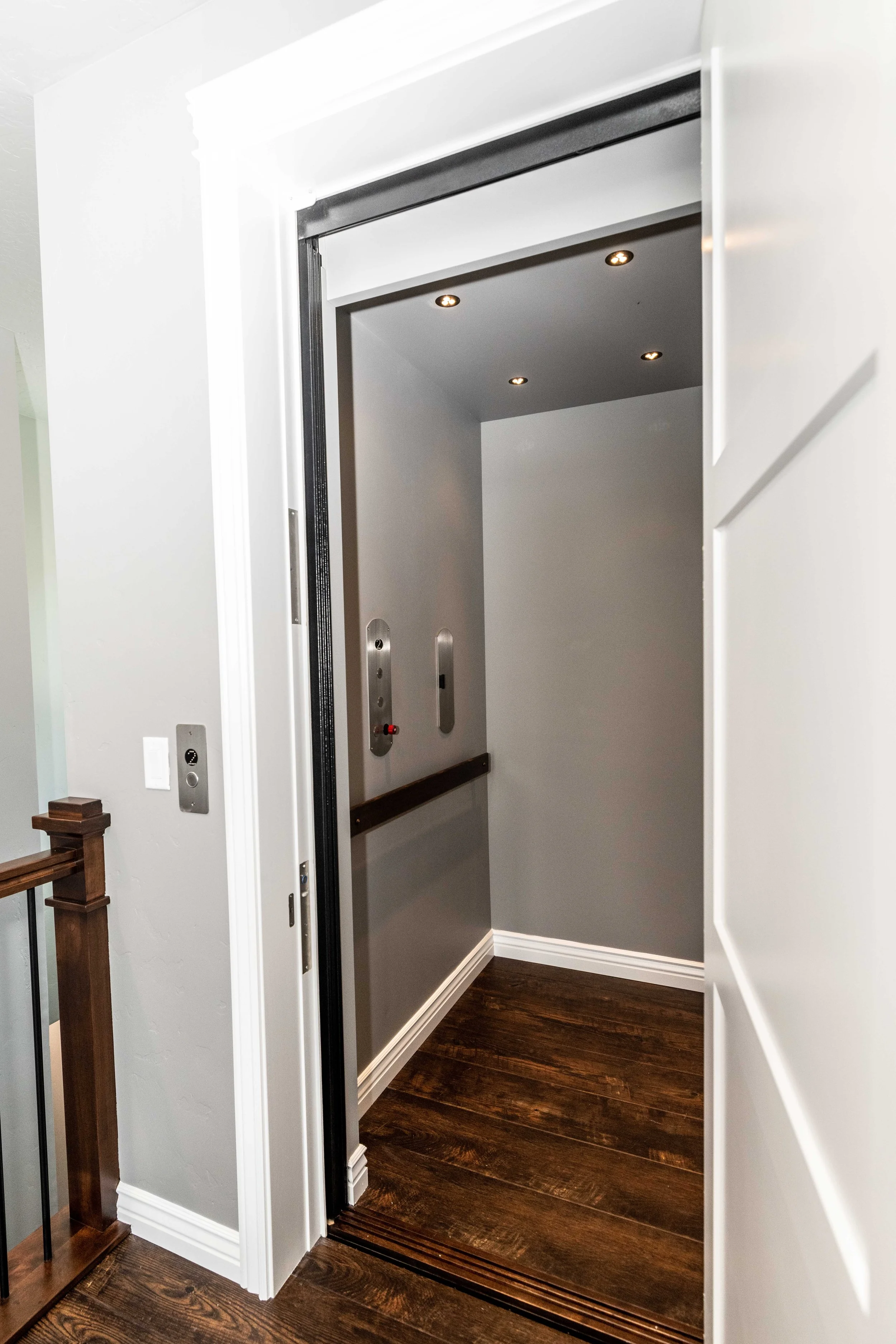 Elevator inside with wooden flooring and gray walls, doors open showing the elevator cabin with controls on the wall.
