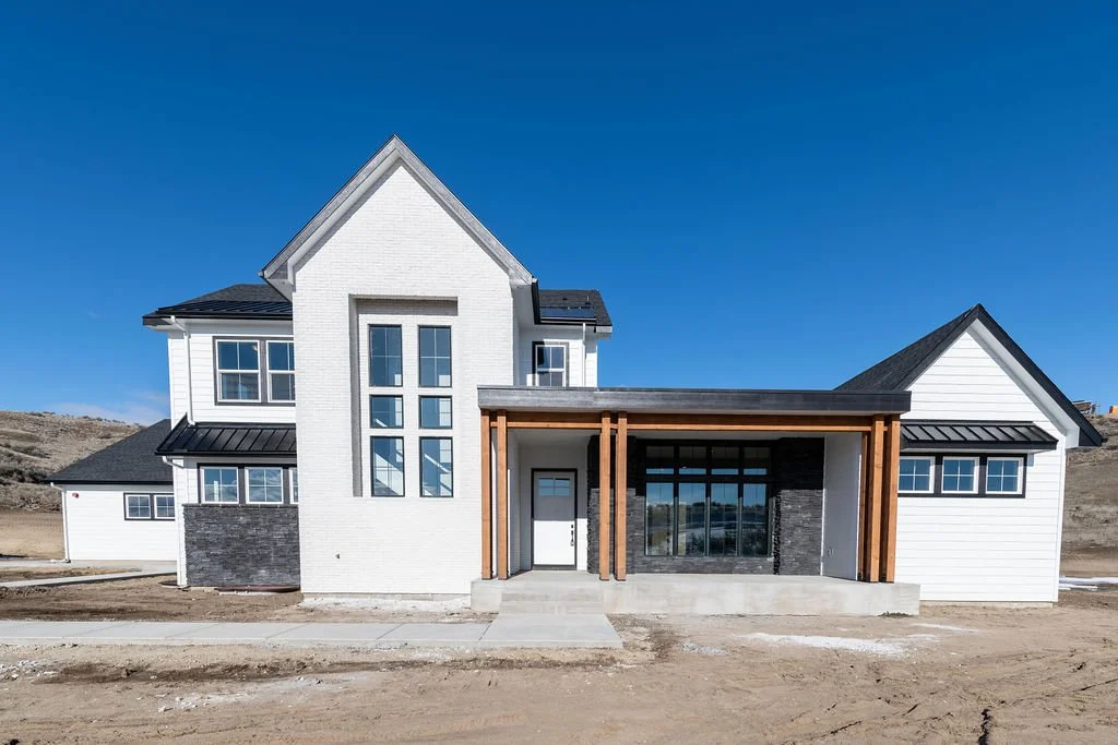 Modern white house with black and wood accents on a dirt lot under a clear blue sky.