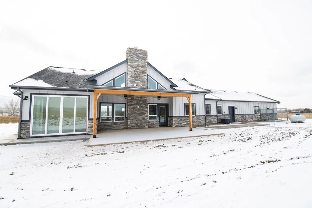 Modern house with a stone chimney and sliding glass doors, situated in a snowy landscape.