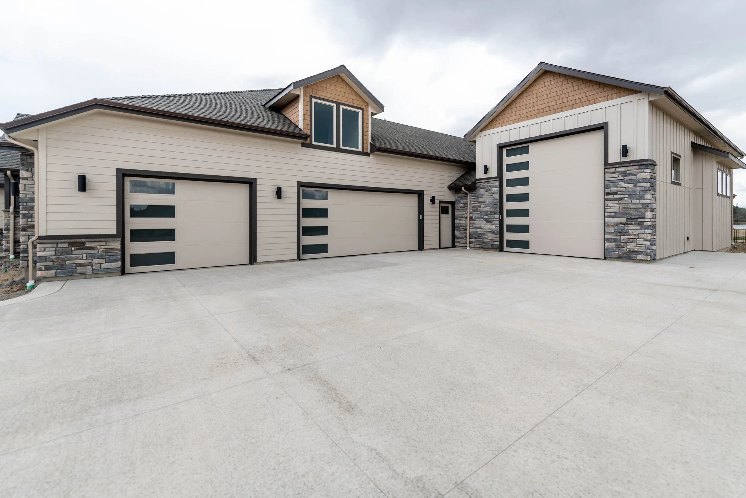 Modern house with three garage doors, stone accents, and a driveway, under cloudy sky.