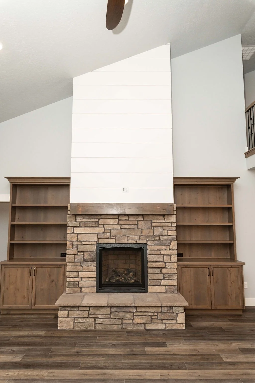 Interior of a living room with a brick fireplace, oak built-in shelves on either side, and a white shiplap wall extending above the hearth, with ceiling and part of a staircase visible.