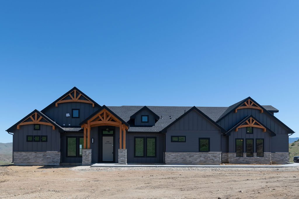 Modern black house with wooden accents, stone foundation, and multiple windows, situated in a barren landscape.