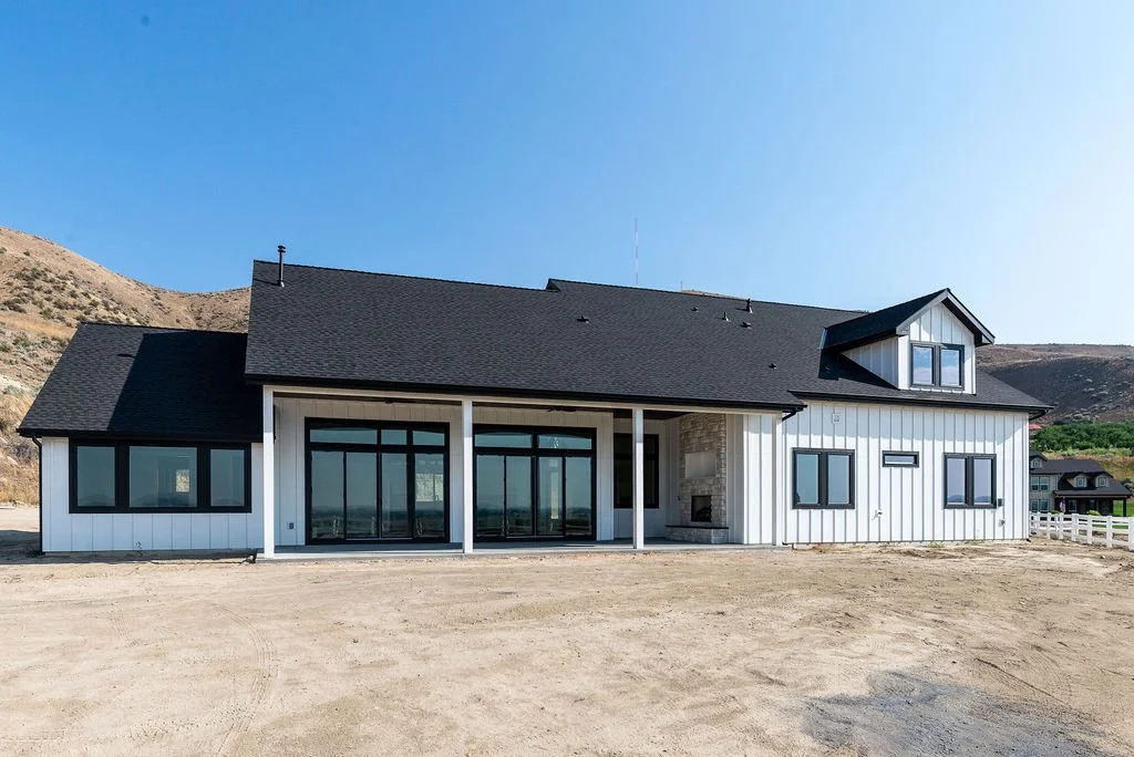 Modern white house with black window frames and a black roof, situated in a barren landscape with hills in the background.