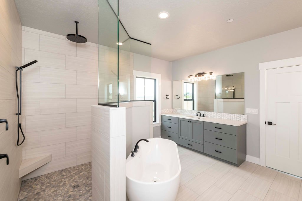 Modern bathroom with a separate walk-in shower with black fixtures, a freestanding bathtub, and a blue-gray vanity with a white hexagonal tile backsplash, large mirror, and two windows.