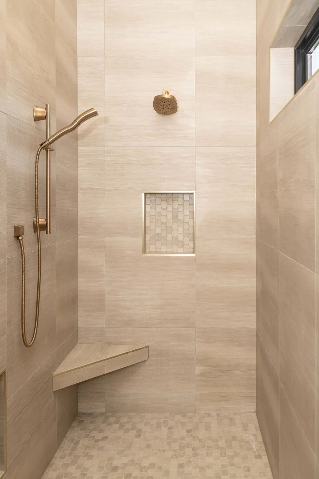 Shower with beige tiles, a built-in shelf with hexagonal tiles, a frameless window, and a rainfall showerhead.
