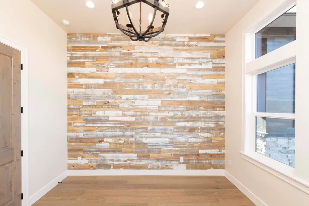 Empty room with a wood accent wall, large window, and a black chandelier ceiling light.