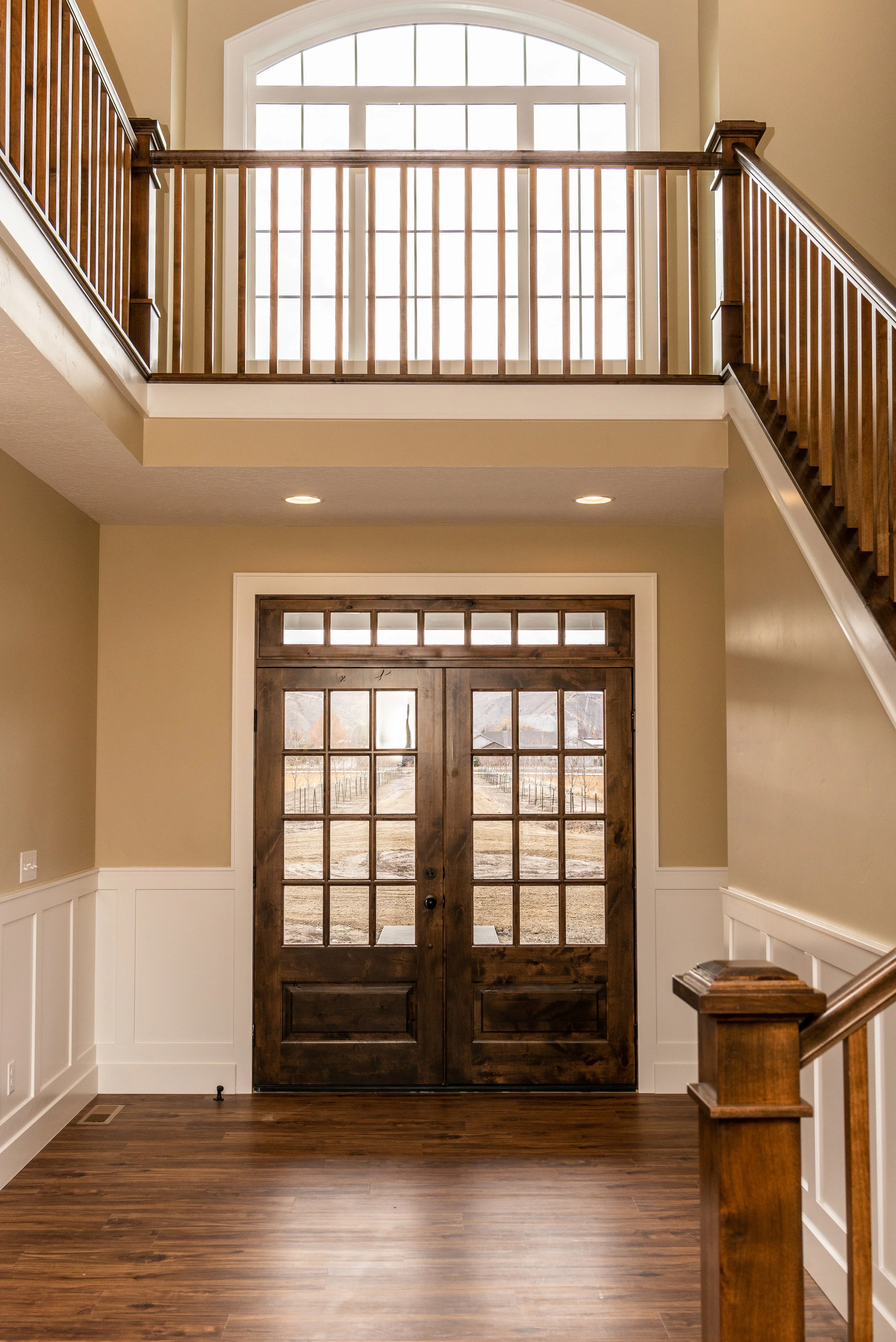Entryway with wooden door and grid of glass panes, with a view outside of a field and trees in the distance.