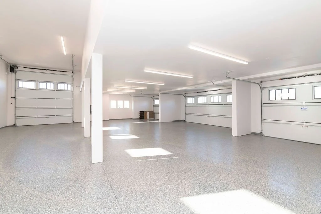 Empty, clean garage with multiple garage doors, white walls, and bright lighting.