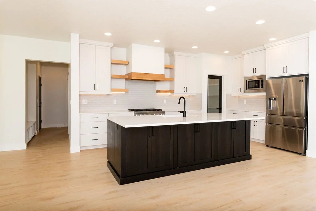 Modern kitchen with white cabinets, black island, stainless steel refrigerator, microwave, and built-in oven, hardwood floors, and recessed lighting.