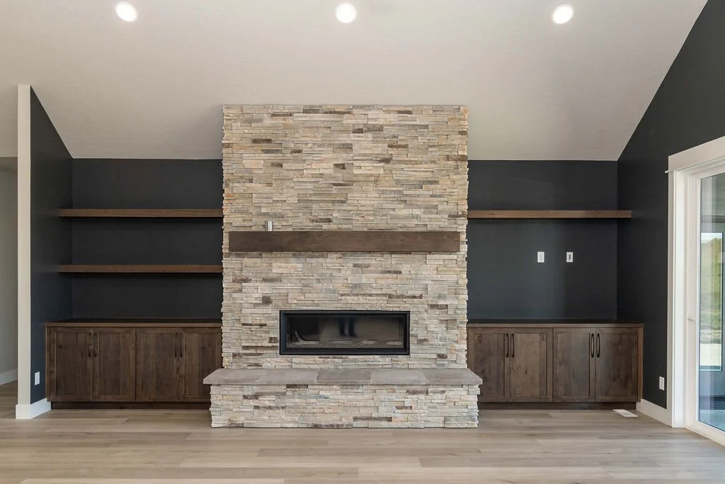 Living room with a stone fireplace, dark gray walls, built-in wooden cabinets, and open shelves on either side.