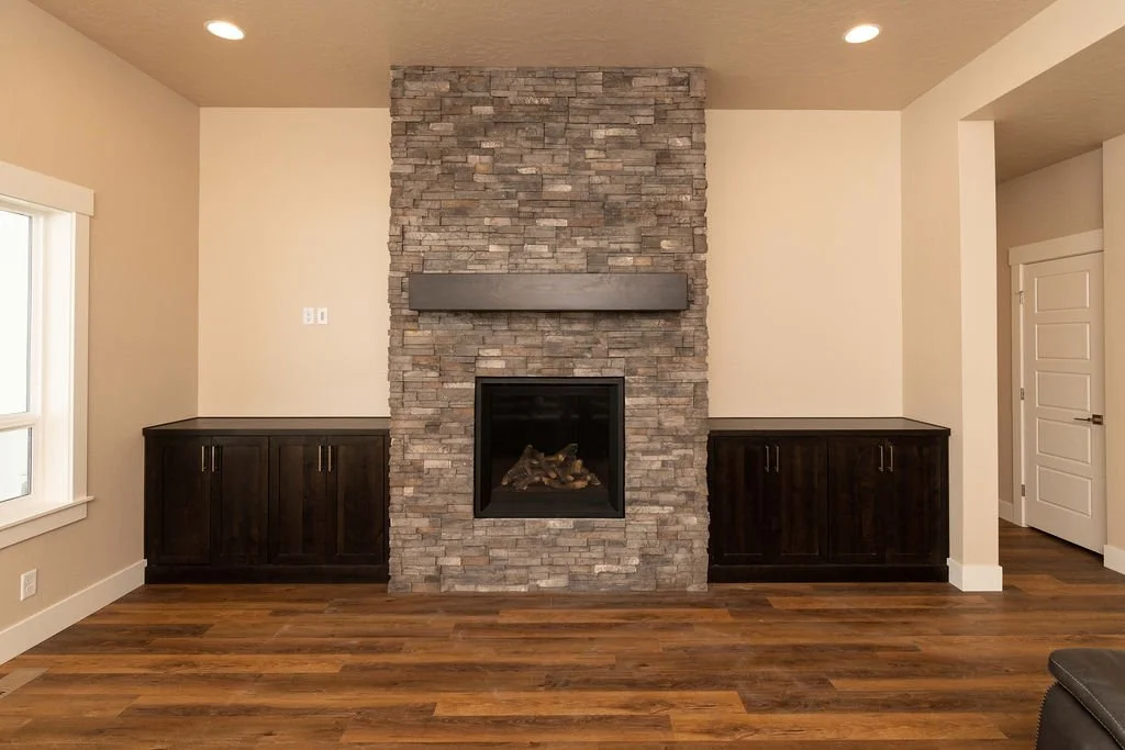 Living room with a stone fireplace, dark wooden cabinets on either side, and hardwood floors.