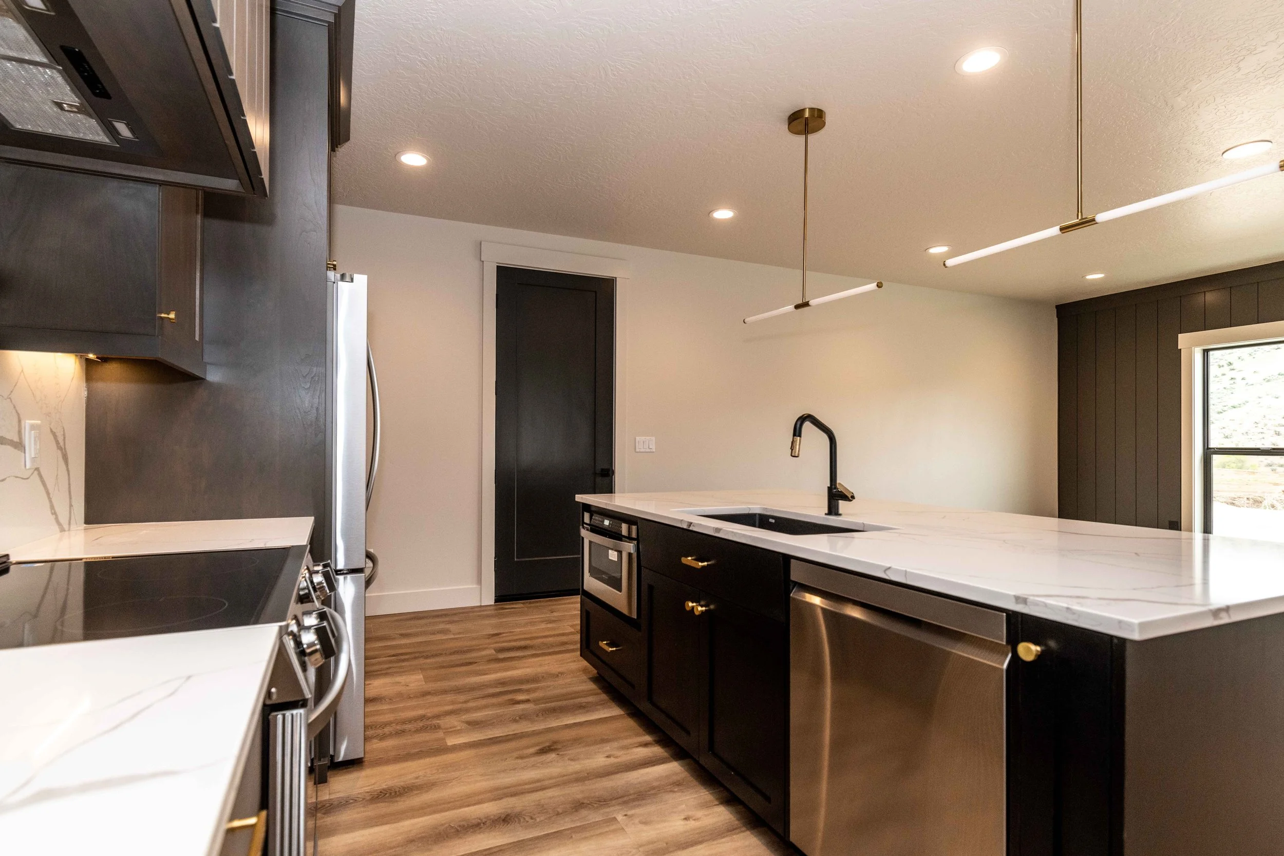Modern kitchen with white marble countertops, black cabinets with gold handles, stainless steel appliances, and pendant lights hanging from the ceiling.