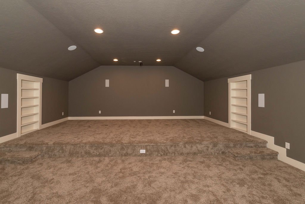 Empty finished attic with gray walls, built-in bookshelves, and brown carpeted floor.