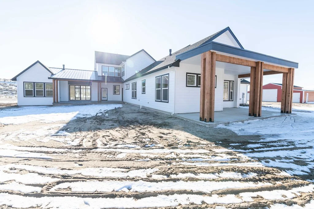 New modern house with white exterior, large windows, wooden beams on the porch, and snow-covered ground.