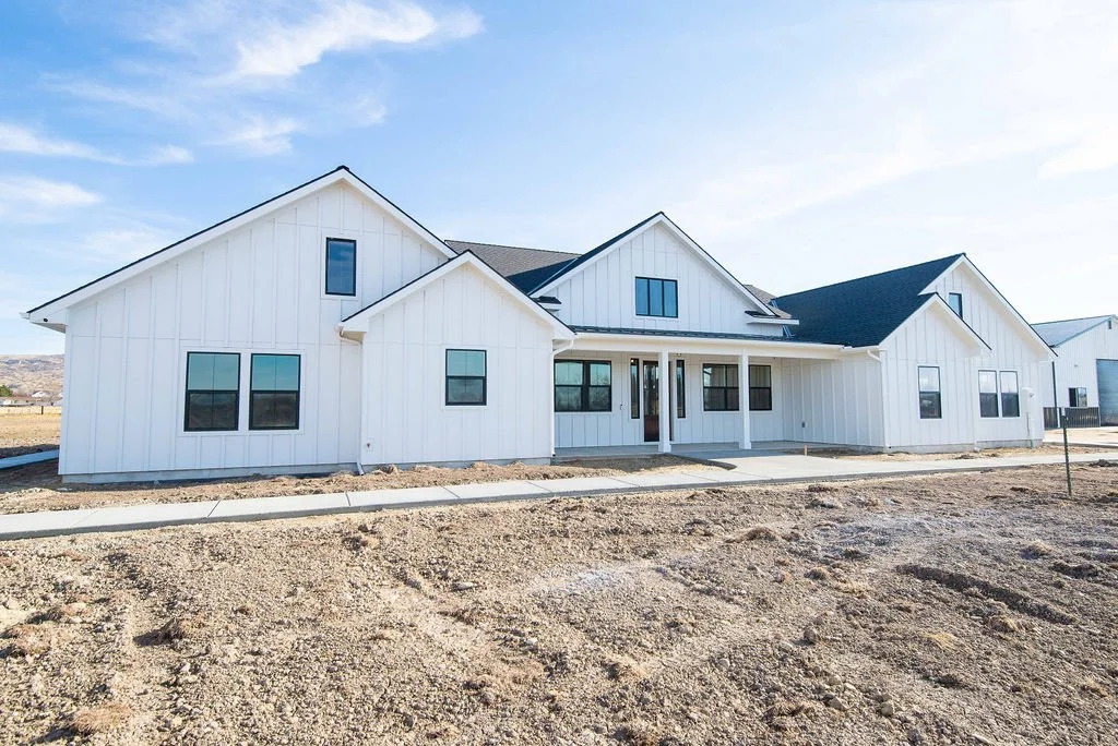 New white house with dark roof, multiple windows, and front porch in a developing neighborhood under blue sky.