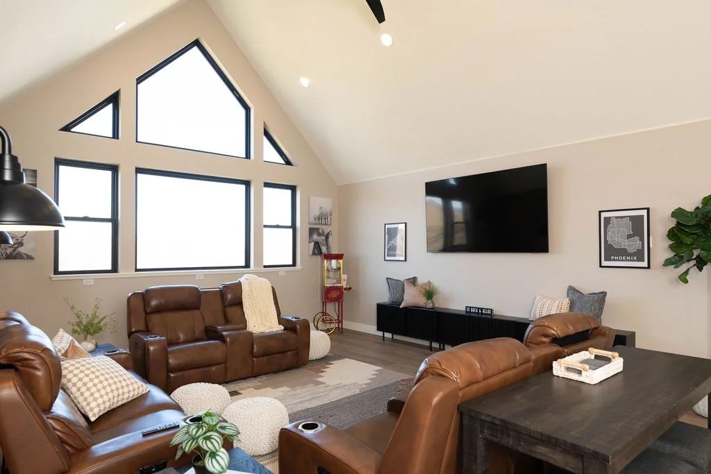 Living room with large triangular window, leather sofas, wall-mounted TV, framed wall art, and a neutral color palette.