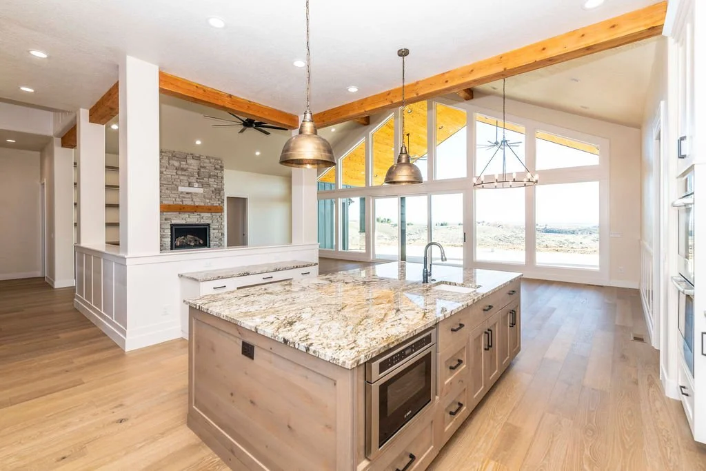 Open-concept kitchen with granite island, wooden flooring, large windows with a view, and modern lighting fixtures.