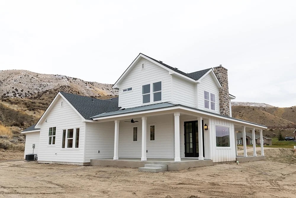 White two-story house with a porch, surrounded by barren land and hills in the background.