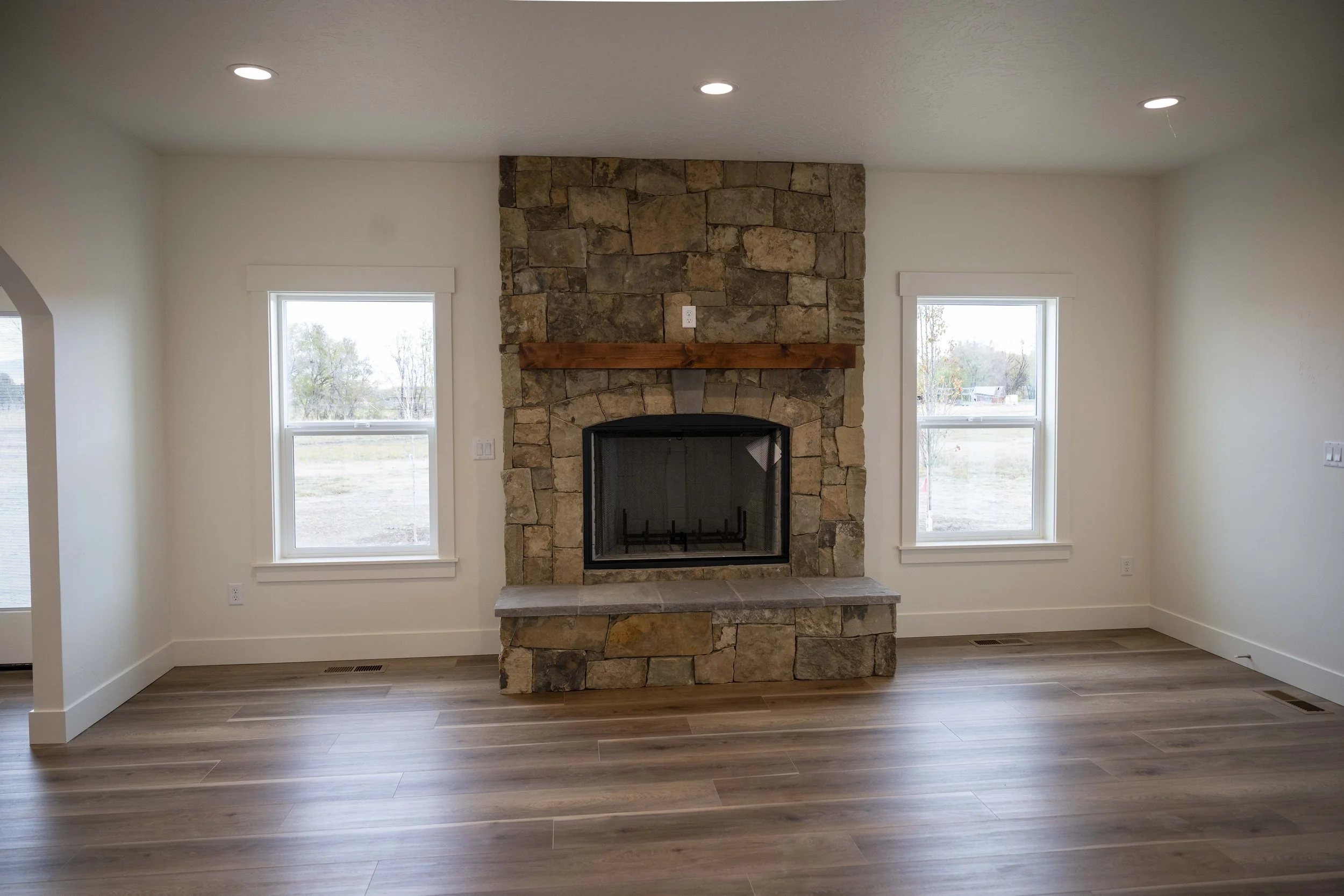 Interior of a living room with a stone fireplace, two windows, and hardwood floors.