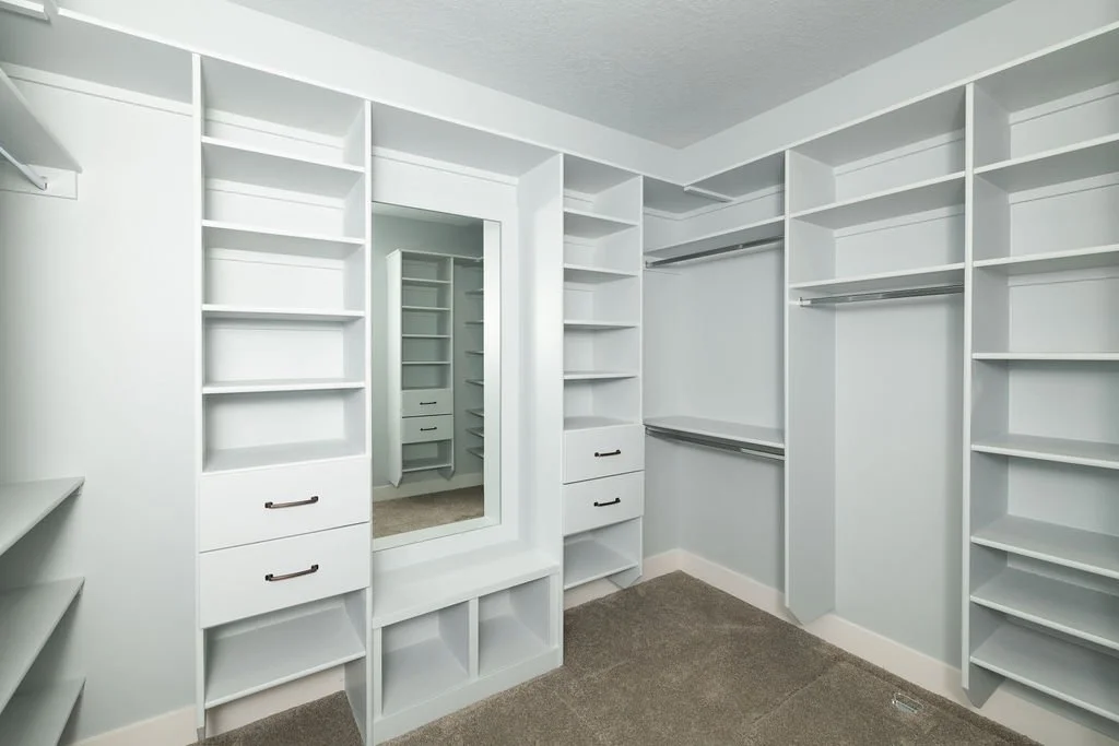 Empty white walk-in closet with multiple shelves, drawers, and hanging rods, with a full-length mirror in the center.