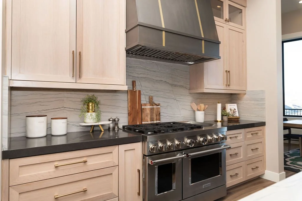 Modern kitchen with light wood cabinets, black countertops, a stainless steel stove, and decorative items on the counter.