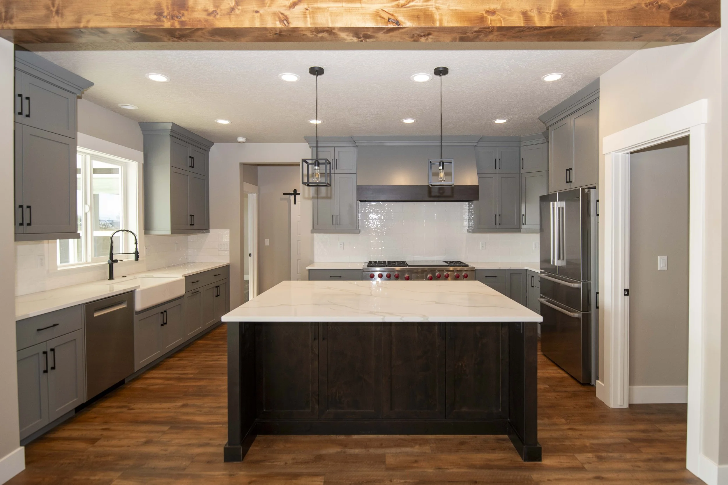 Modern kitchen with gray cabinets, stainless steel appliances, a large white marble island, and pendant lighting.
