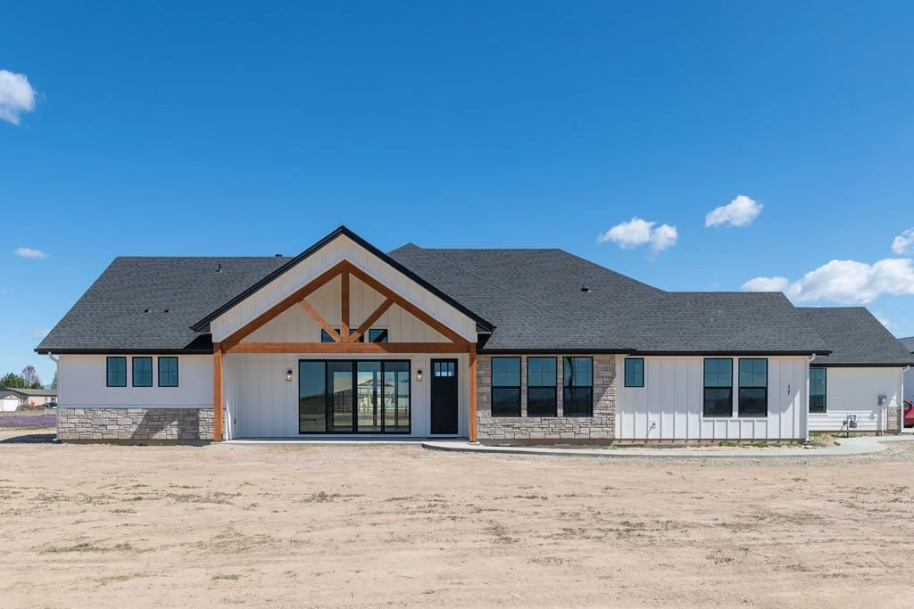 New modern house with white siding, stone accents, and a dark gray roof under a blue sky.