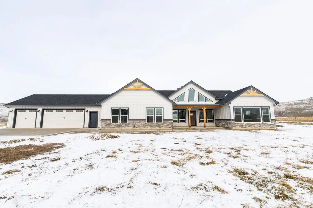 Modern house with white siding, stone accents, large windows, and attached garage surrounded by snow on a cloudy day.