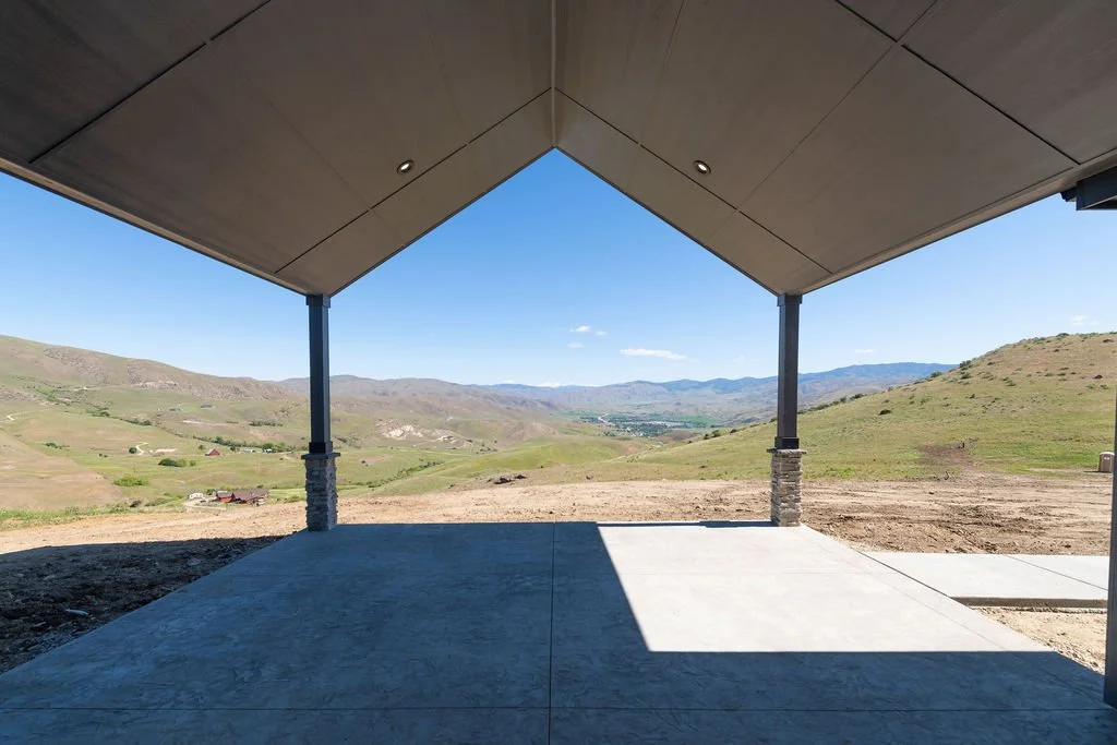 View from underneath a covered patio overlooking a scenic green valley and rolling hills.