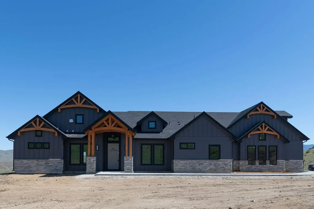 New modern house with black exterior, stone accents, and wooden trim under a clear blue sky.