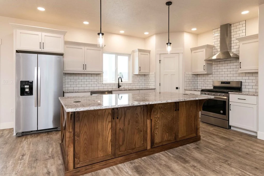 Modern kitchen with white cabinets, stainless steel refrigerator and oven, wooden island, white subway tile backsplash, and pendant lighting.