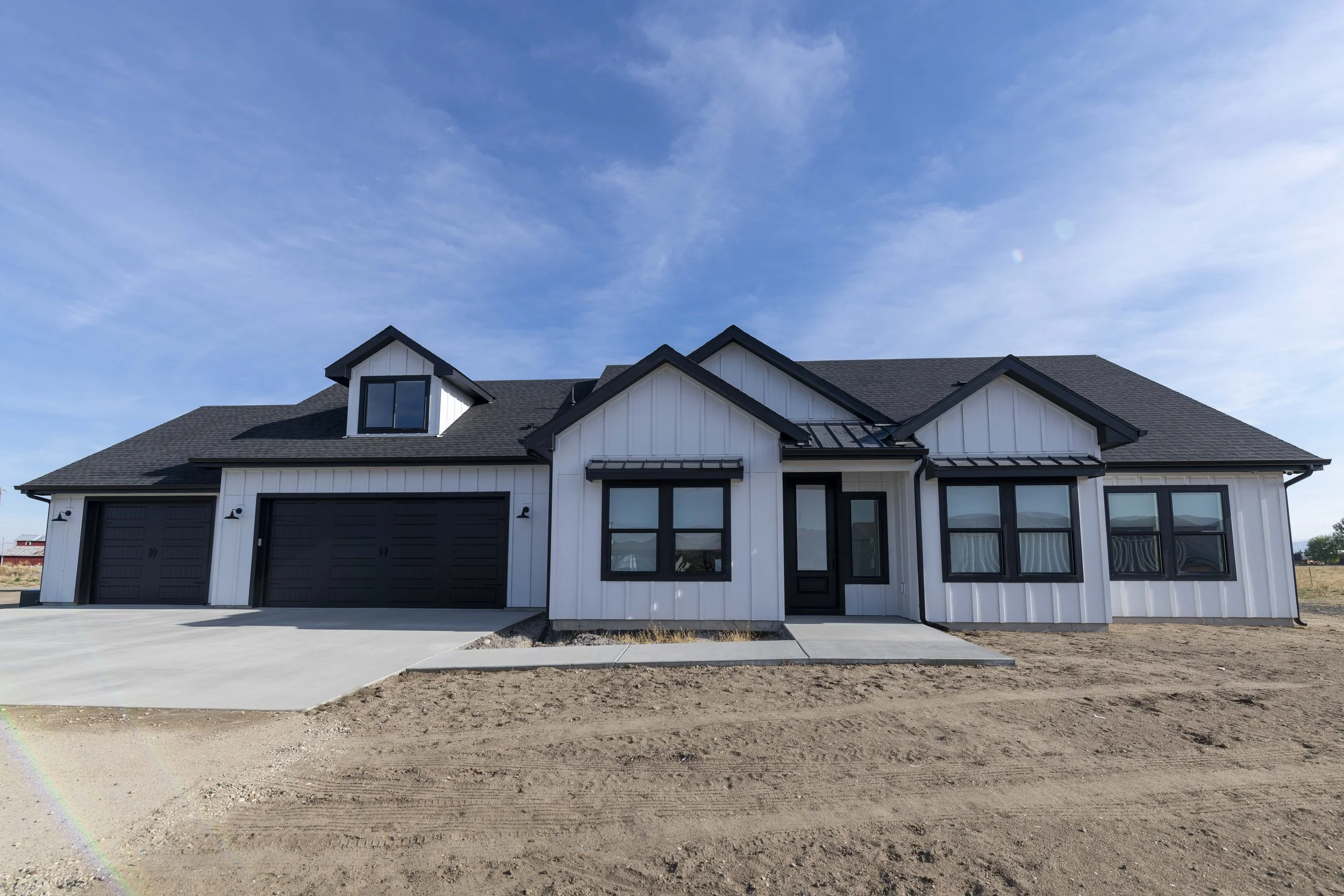 A modern two-story house with white exterior siding, black trim, and black garage doors under a blue sky with some clouds.