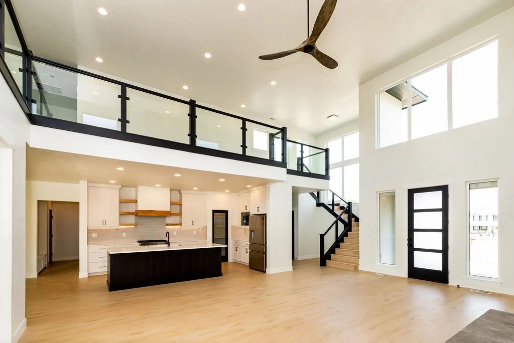 Modern open-concept living room and kitchen with high ceilings, large windows, a staircase, and a ceiling fan.