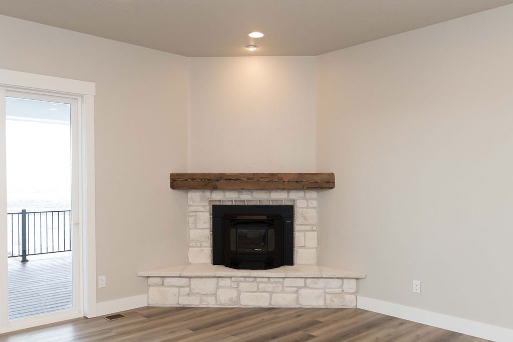 Living room corner with a white brick fireplace, wooden mantel, sliding glass door to a balcony, and hardwood floors.