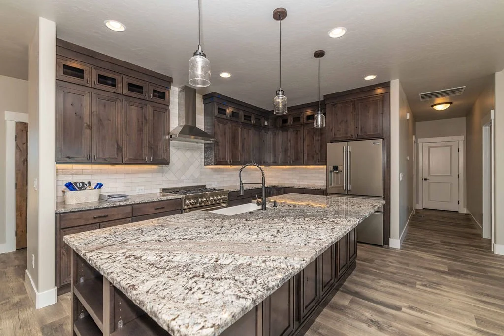 Modern kitchen with dark wood cabinets, granite countertops, stainless steel appliances, pendant lighting, and a tile backsplash.