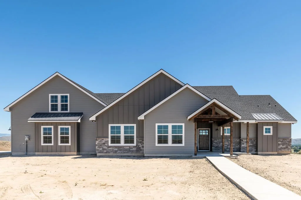 A new modern house with gray siding, stone accents, and a dark roof, under a clear blue sky.