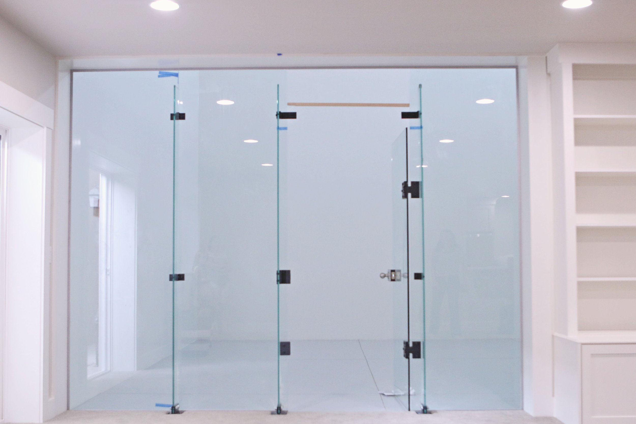 A glass door with black hardware and a metal handle in a modern indoor space, with white walls and shelves on the right.