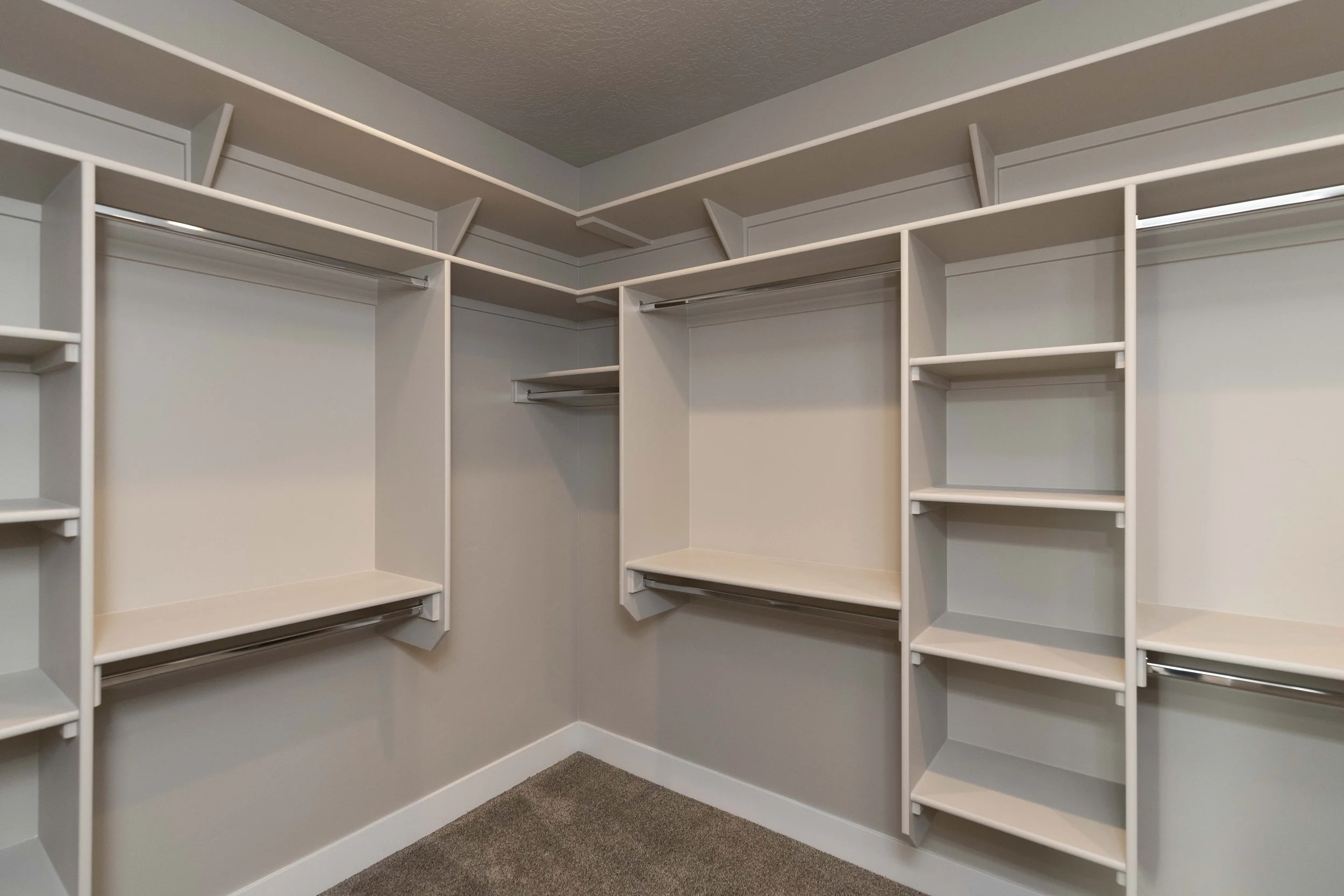 Empty white walk-in closet with built-in shelves, hanging rods, and beige carpeted floor.