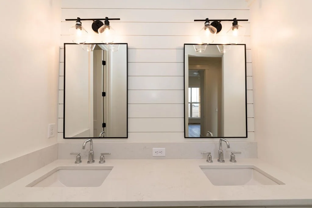 Double bathroom vanity with two sinks, two rectangular mirrors, and black light fixtures on a white shiplap wall.