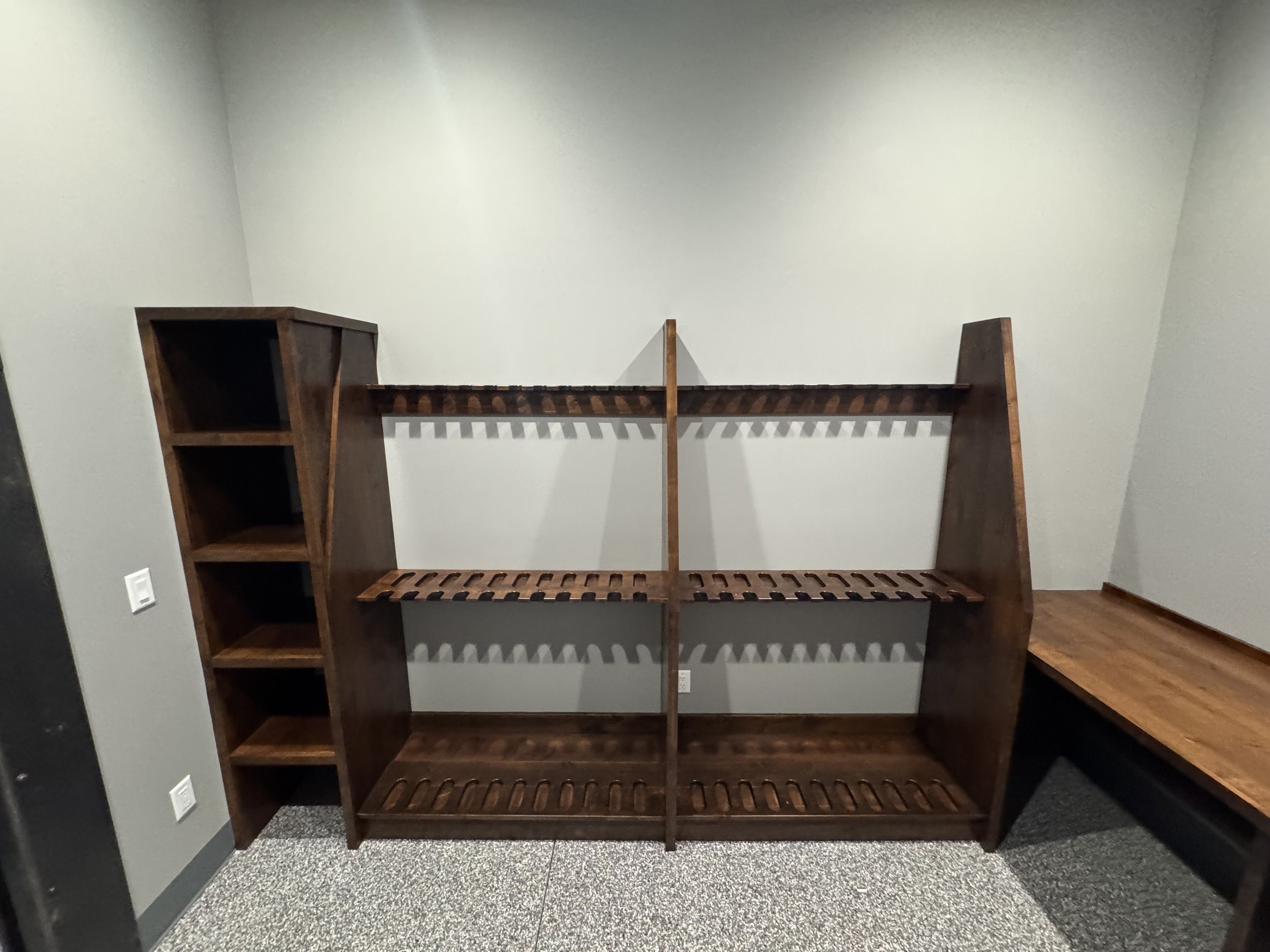 Empty wooden bookshelf with multiple shelves against a light gray wall in a room with gray carpeting.