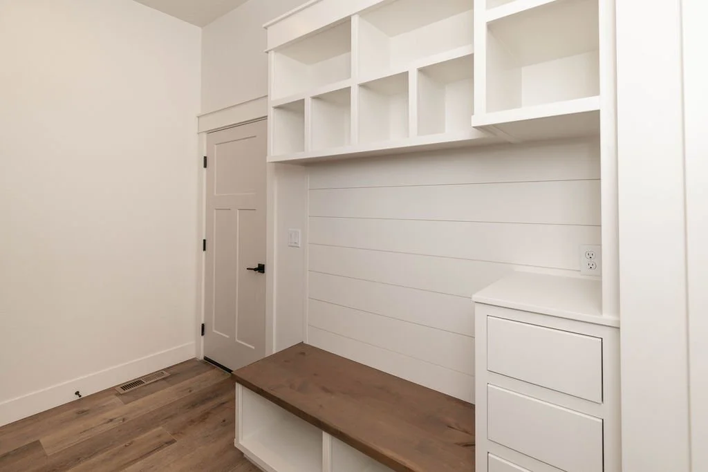 White built-in shelving and seating area in a room with wooden flooring and a closed door.