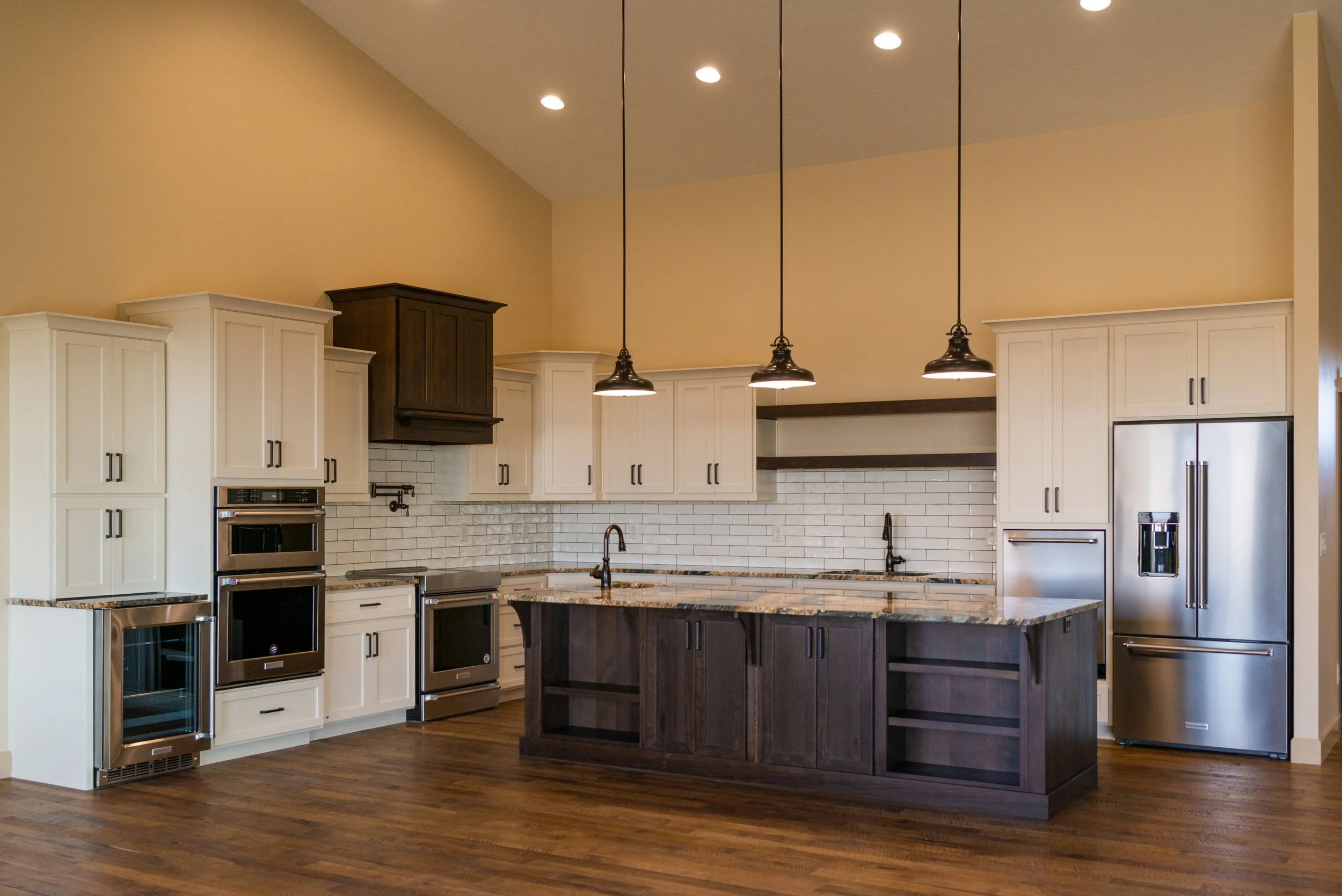 A modern kitchen with white and dark wood cabinets, stainless steel appliances, a marble countertop island, pendant lighting, and a white subway tile backsplash.