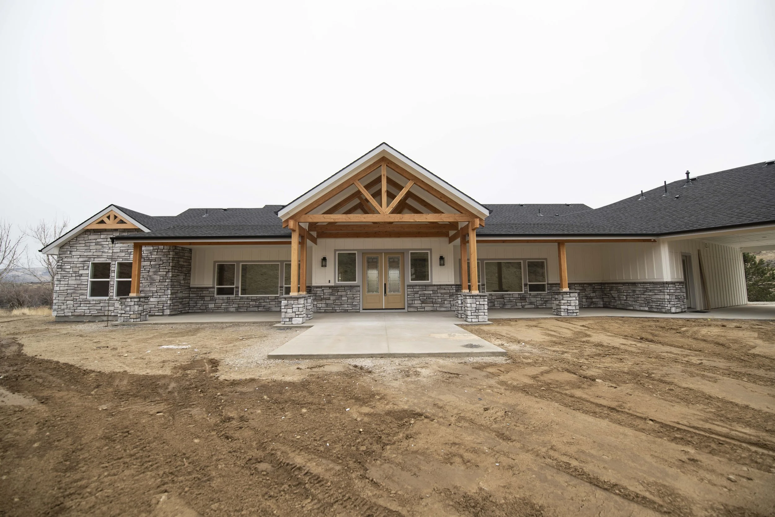 Front view of a newly built house with stone and siding exterior, gabled roof, covered porch, and surrounding dirt yard.