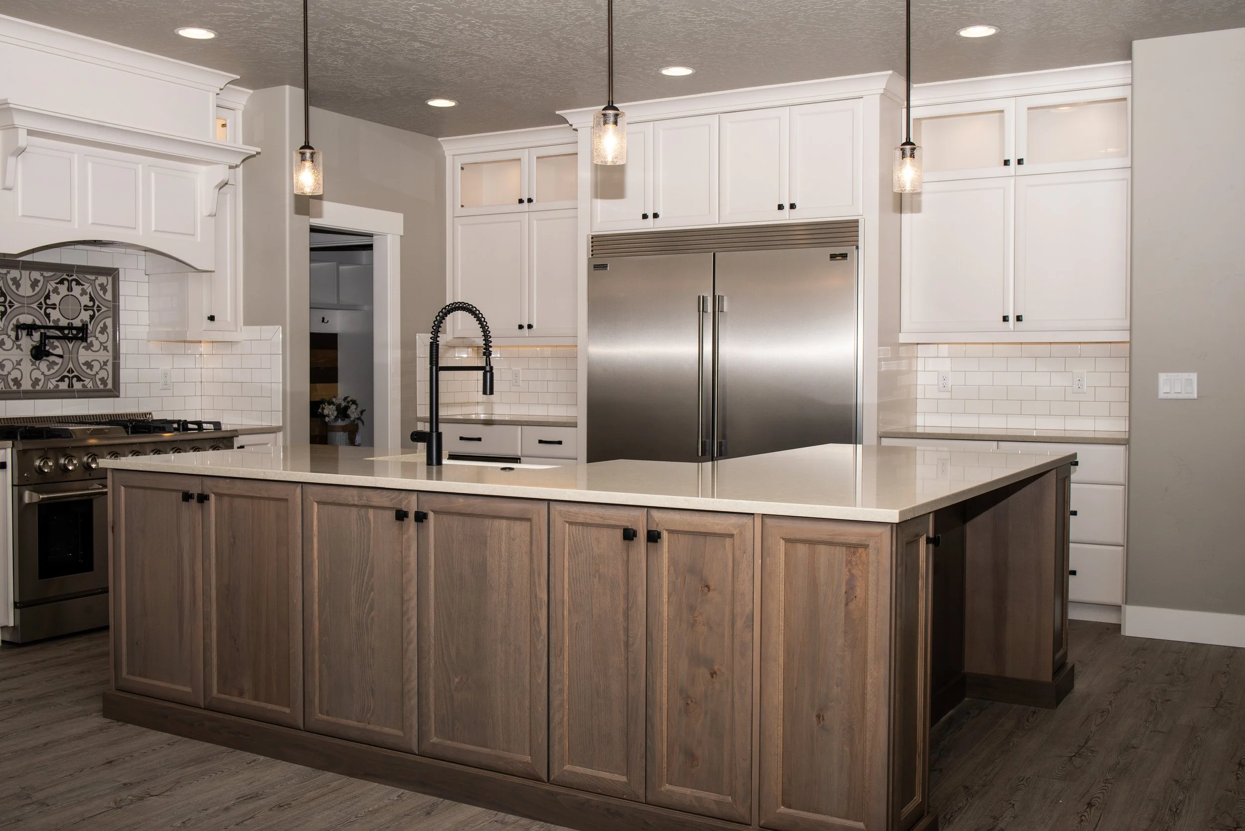Modern kitchen with white upper cabinets, a large stainless steel refrigerator, an island with wood paneling, black hardware, a black pull-down kitchen faucet, and pendant lights.