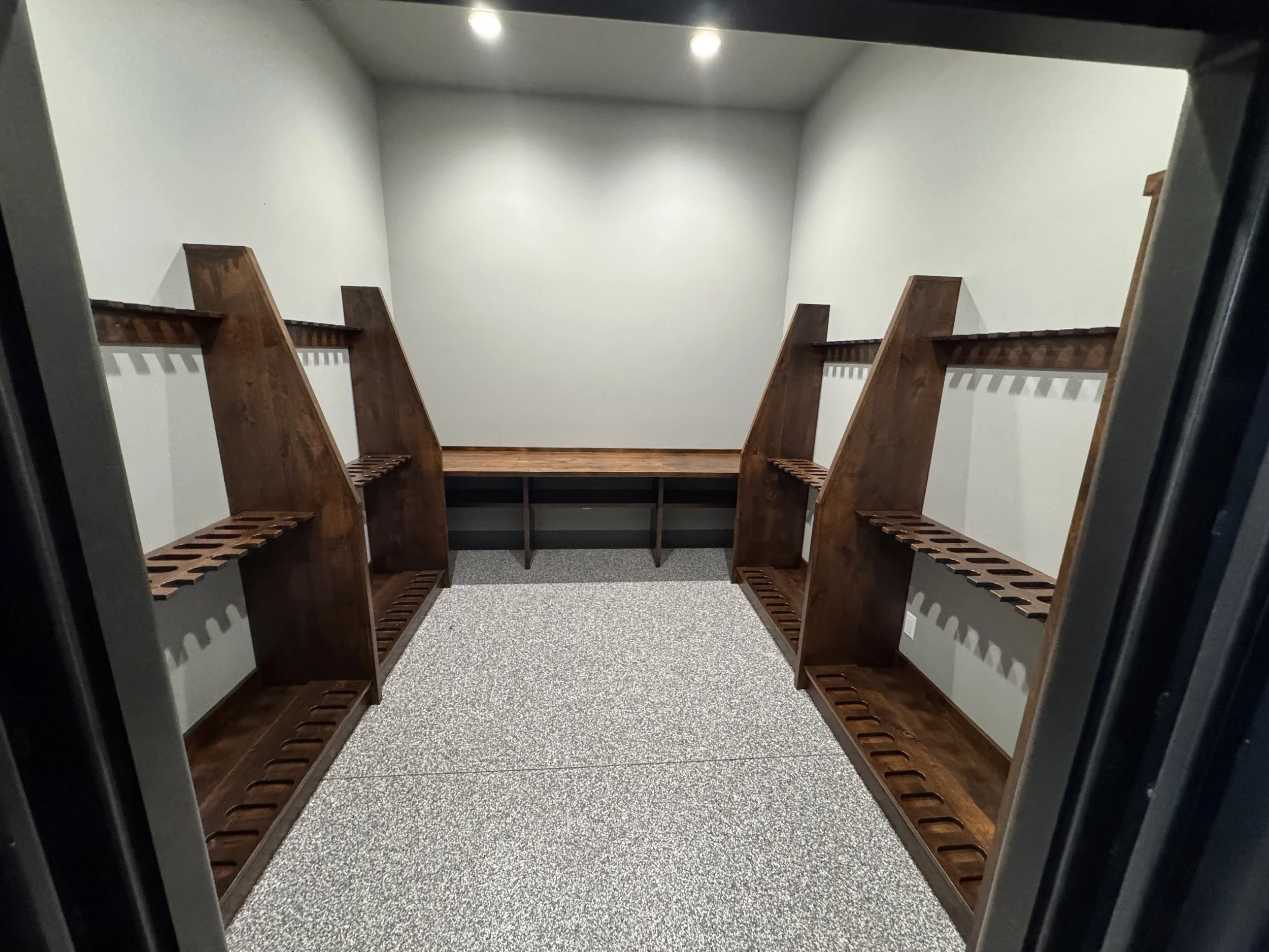 A hallway with wooden benches on both sides, white walls, a carpeted floor, and ceiling lights.